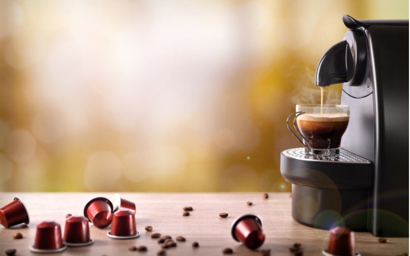 Kapslový kávovary - kávovar při přípravě nápoje a kapsle na dřevěném stole