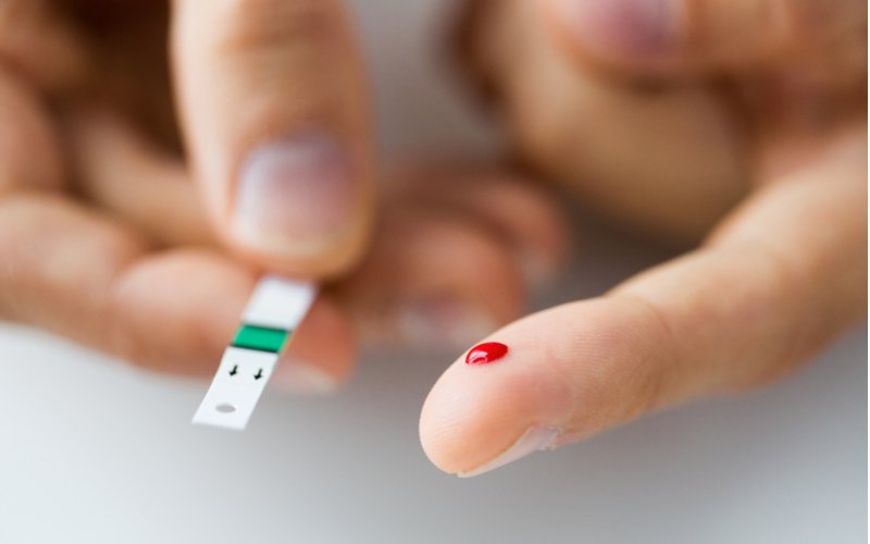 Kapka krve na prstu a testovací proužek